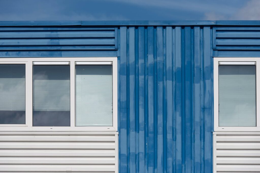 Close-up of a blue industrial building facade with two windows and metal siding under clear sky.