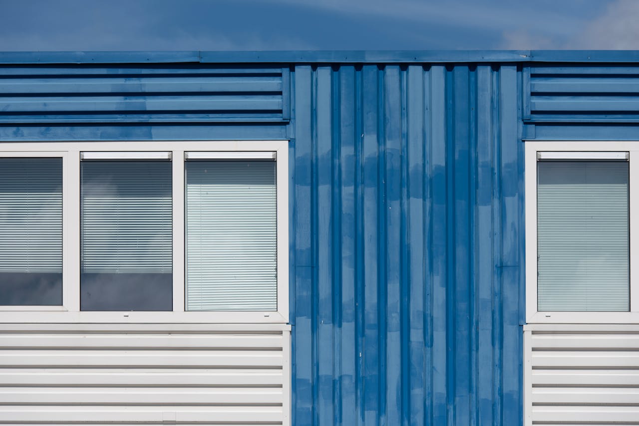 Close-up of a blue industrial building facade with two windows and metal siding under clear sky.